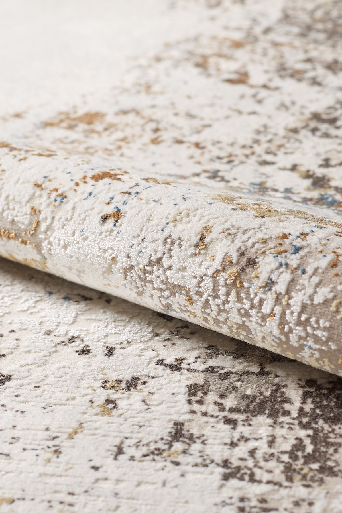 A close-up of the Sandy Papyrus Canvas Area Rug - M679L shows its soft, plush surface and modern machine-made design, featuring a beige base with brown, gold, gray, and blue abstract patterns.