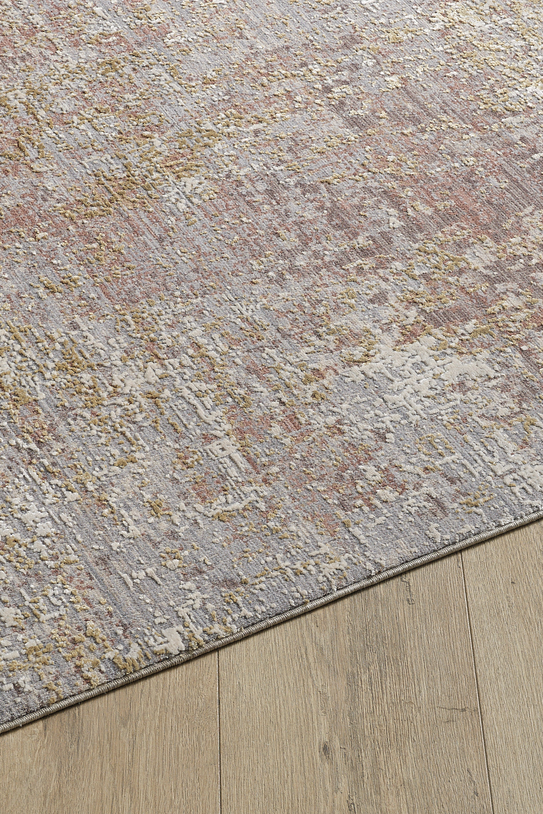 A close-up of the Sandy Whisper Neutral Rug - M628M, a machine-made rug featuring textured gray, taupe, and gold tones, displayed on a wooden floor.