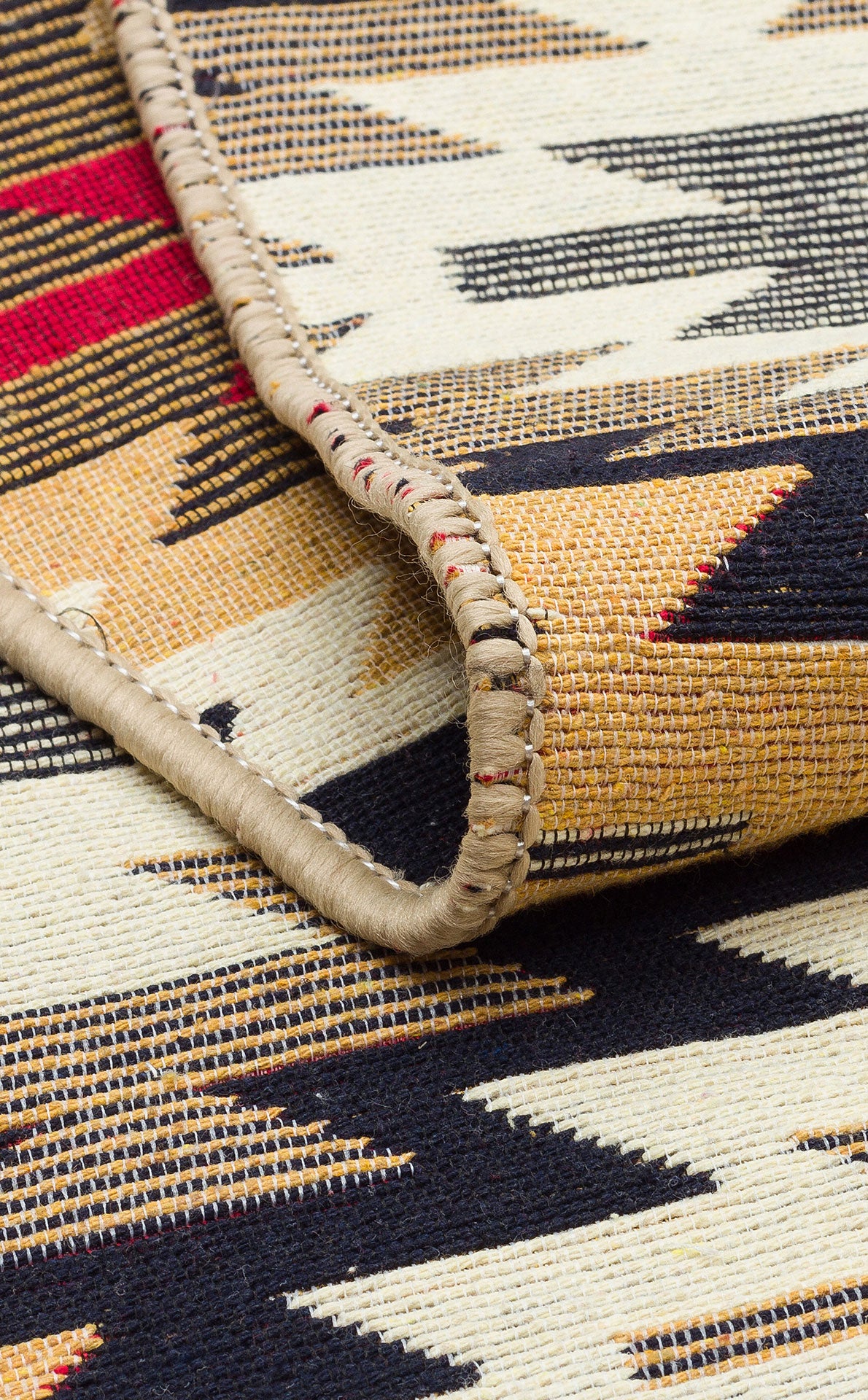 A close-up of the Scarlet Path - Washable Double-Sided Kilims - AR33 rug displays a bold black, gold, red, and cream geometric pattern with hand-stitched binding revealed along the folded edge.