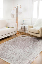 A modern living room with a beige sofa, light armchair with a white fur throw, small round side table with a flower vase, two globe floor lamps, and the Sea Spray - Washable Rug - JR847 (Custom Size) in gray over wood flooring.
