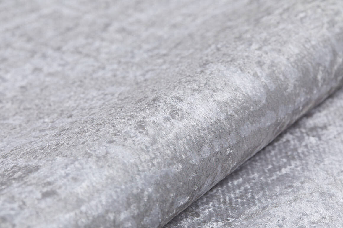 Close-up of the Sea Spray - Washable Rug - JR847 (Custom Size) in light grey velvet with a soft, subtly shiny texture and irregular patterns. Plush material, reminiscent of cream and beige rugs, is folded to highlight its smooth surface.