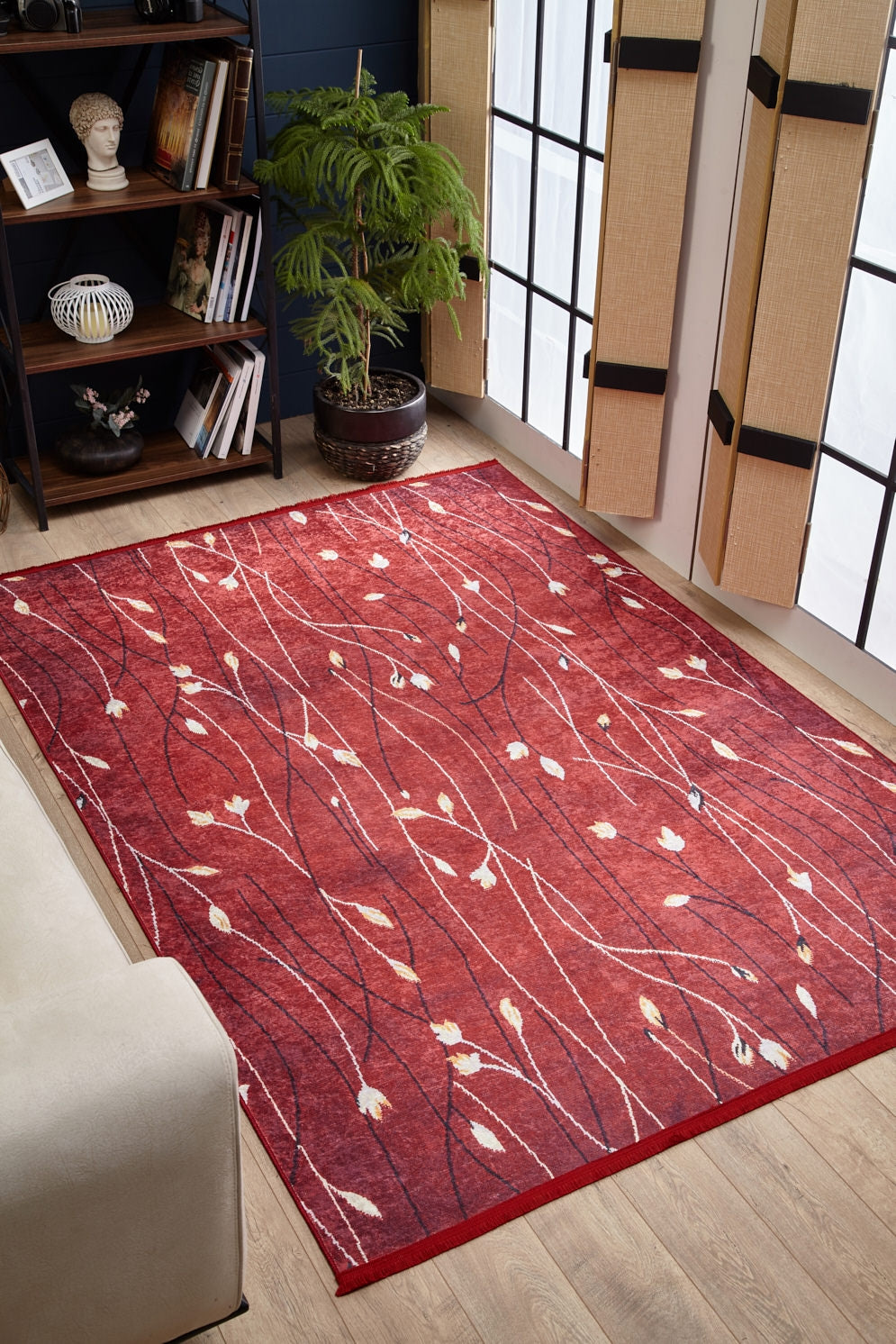 The Secret Garden - Washable Rug - JR1656 features a nature-inspired red, cream, and dark pattern with leaf shapes, shown on a wooden floor near a white sofa—perfect as a washable rug for high-traffic spaces. Custom sizes available.