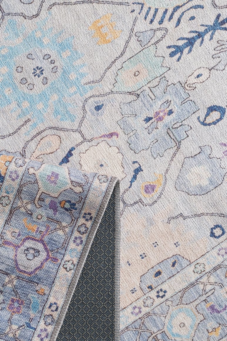 A close-up of the Seraphix Pastel Bordered Washable Rug (LCC3011) in blue, cream, and pastel hues with floral and geometric patterns; a folded corner shows its dark non-slip backing—perfect for high-traffic areas.