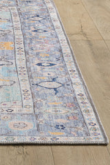 A close-up of the Seraphix Pastel Bordered Washable Rug - LCC3011 shows its rectangular, pastel blue design with a decorative border on light wood flooring—perfect for high-traffic areas with soft beige and pink intricate details.