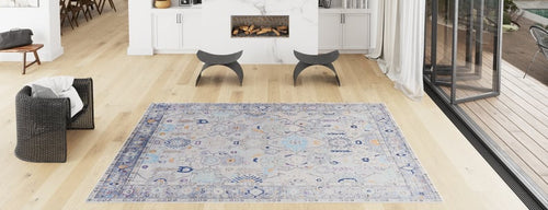 Bild 1 in Galerieansicht laden. A spacious, modern living room with light wood floors, a Seraphix Pastel Bordered Washable Rug (LCC3011) ideal for high-traffic areas, a black woven chair, two gray stools by the fireplace, and floor-to-ceiling windows welcoming natural light.
