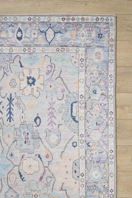 Bild 1 in Galerieansicht laden. The image shows the Seraphix Pastel Bordered Washable Rug - LCC3011 (Custom Size), featuring blue, cream, and lavender floral and geometric motifs, ideal for high-traffic areas, placed on a light wood floor.