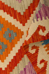 A close-up of the Silk Road - Handwoven Kilim (Outlet) US, featuring geometric patterns in vibrant hues. The flatweave rug is partially folded, showcasing its intricate handwoven design and richly textured surface.