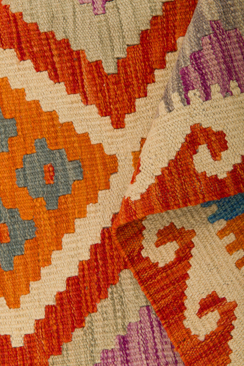 Load image 1 in gallery view. A close-up of the Silk Road - Handwoven Kilim (Outlet) US, featuring geometric patterns in vibrant hues. The flatweave rug is partially folded, showcasing its intricate handwoven design and richly textured surface.
