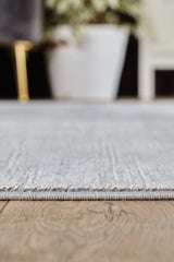 Close-up of the edge of the Silver Lining Grey Rug - M352I on a wooden floor, with a white plant pot and blurred background furniture visible in the distance.