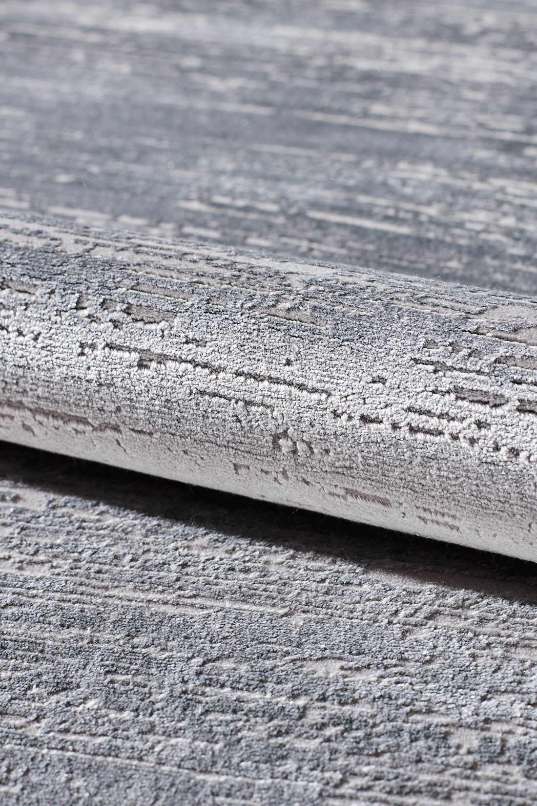 A close-up of the Silver Lining Grey Rug - M352I, featuring a rolled edge and modern abstract pattern in grey and white, reminiscent of rough brushstrokes.