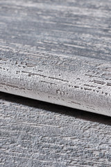 A close-up of the Silver Lining Grey Rug - M352I, featuring a rolled edge and modern abstract pattern in grey and white, reminiscent of rough brushstrokes.