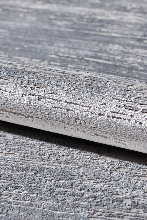 Load image 1 in gallery view. A close-up of the Silver Lining Grey Rug - M352I, featuring a rolled edge and modern abstract pattern in grey and white, reminiscent of rough brushstrokes.