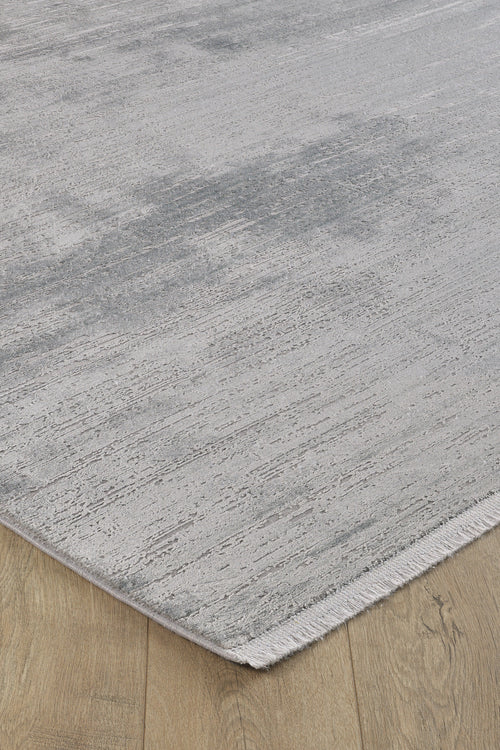 Load image 1 in gallery view. A close-up of the corner of the Silver Lining Grey Rug - M352I on a wooden floor, highlighting its subtle patterns and short fringe along the edge.