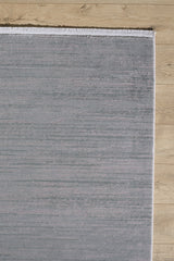 The Silver Lining Grey Rug - M352I is a rectangular, light gray minimalist rug with a flat pile and short white fringe on the top edge, shown partially on a light wood floor with the rest of the floor visible.