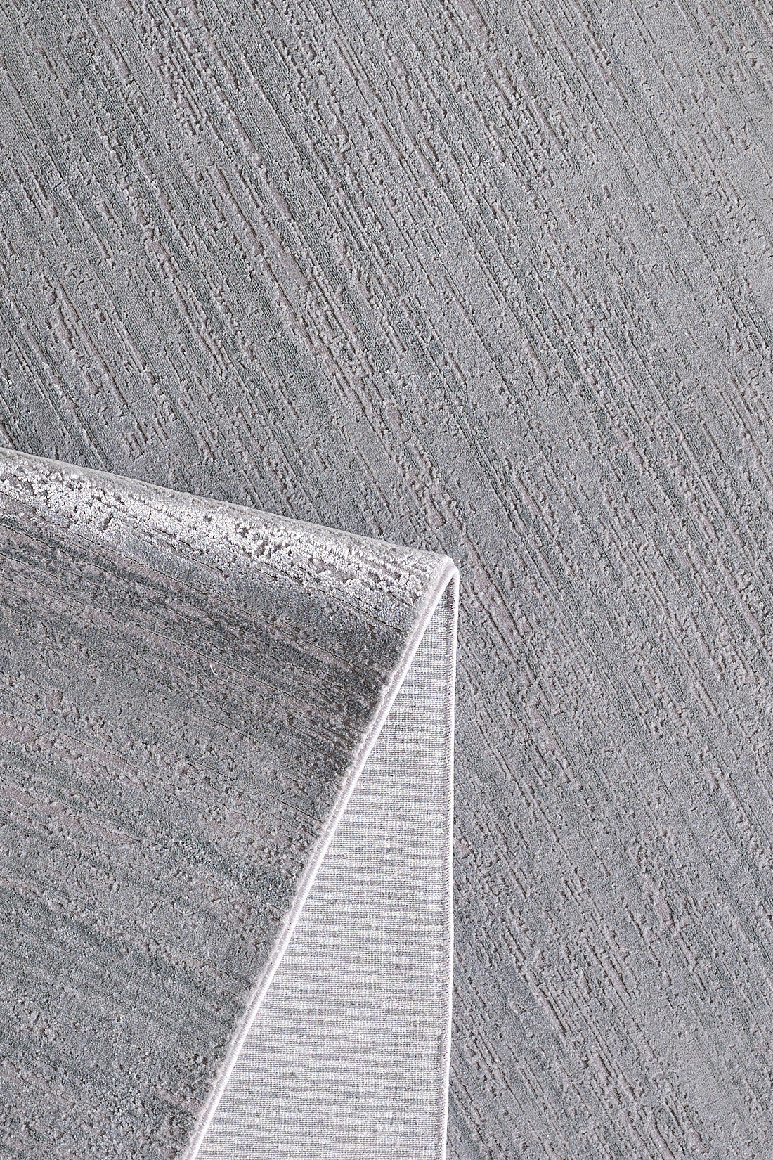 A close-up of the Silver Lining Grey Rug - M352I shows its textured flat pile with diagonal lines. A folded corner reveals its thickness and weave, while the subtle pattern makes it ideal for minimalist decor.