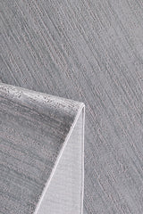 A close-up of the Silver Lining Grey Rug - M352I shows its textured flat pile with diagonal lines. A folded corner reveals its thickness and weave, while the subtle pattern makes it ideal for minimalist decor.