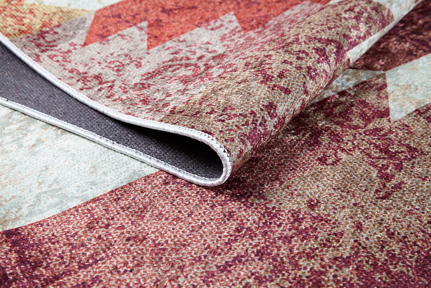 A close-up of the Simplistic Artistry - Washable Rug - JR1647 (Custom Size) reveals its red, beige, and gray pattern with one corner lifted to show the texture, thickness, and washable underside—perfect for high-traffic areas.