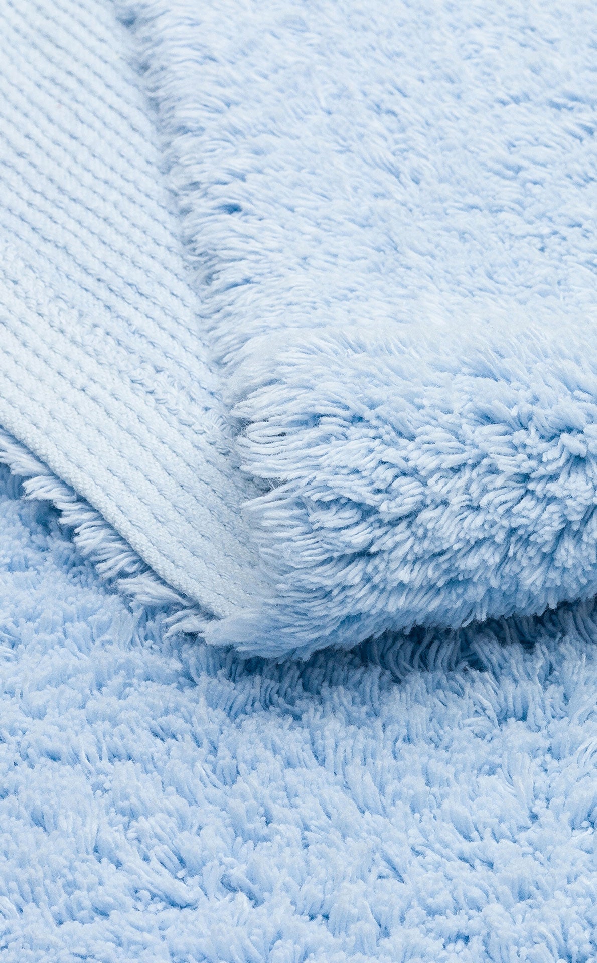 A close-up of the Sky Nap - Washable Shaggy - CBNPLAIN rug displays its soft blue, plush cotton texture and cozy thickness, with a neatly folded corner highlighting its shaggy surface.