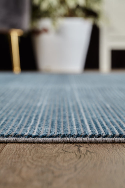 Load image 1 in gallery view. Close-up of the Slate to Midnight Navy Rug - M497M with blue stripes on a wooden floor, featuring a white plant pot and softly blurred green foliage in the background.