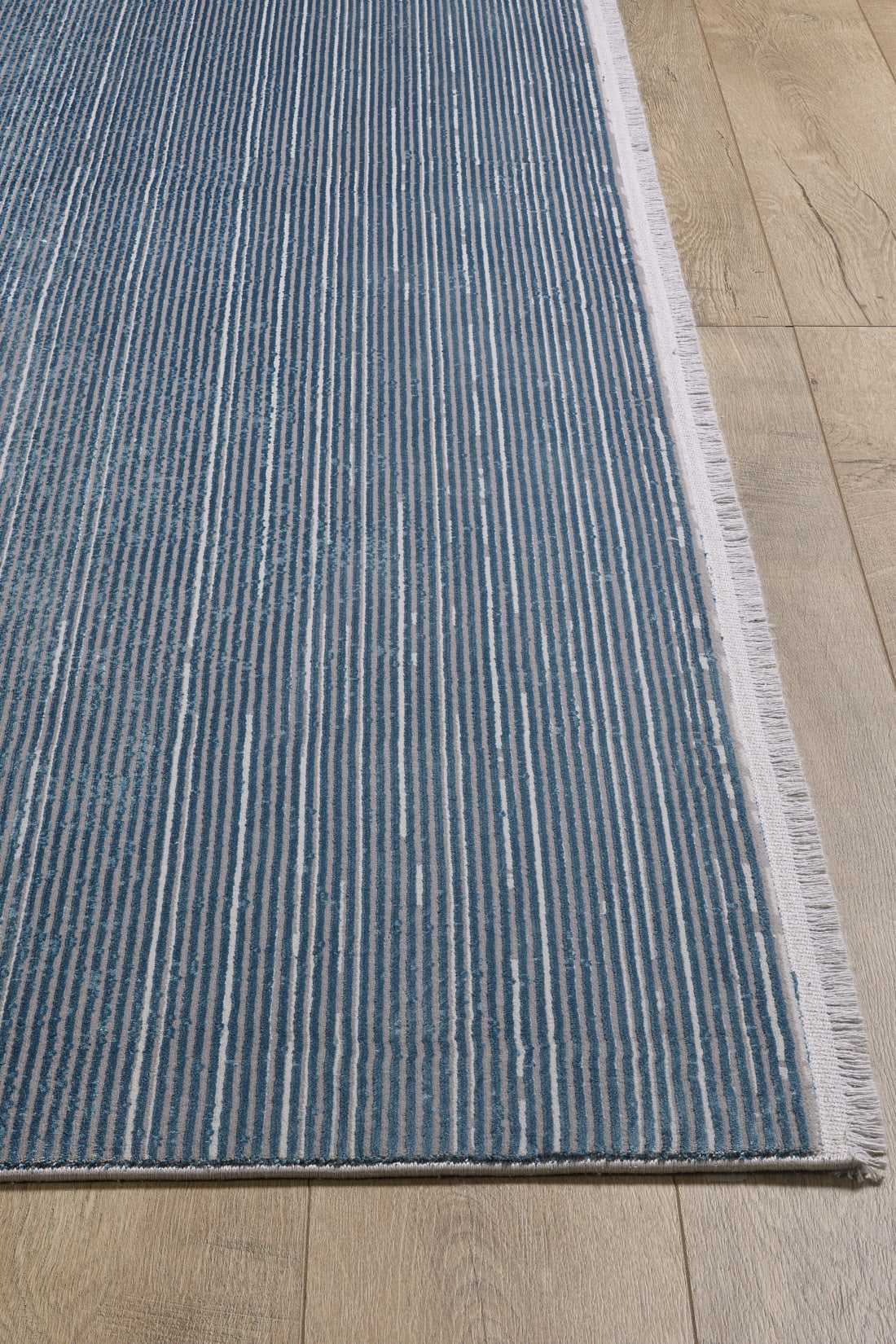 The Slate to Midnight Navy Rug - M497M is a contemporary machine-made area rug in blue and white stripes with fringe on one edge, shown laid on a light wooden floor. The stripes run parallel to the rug's shortest side.