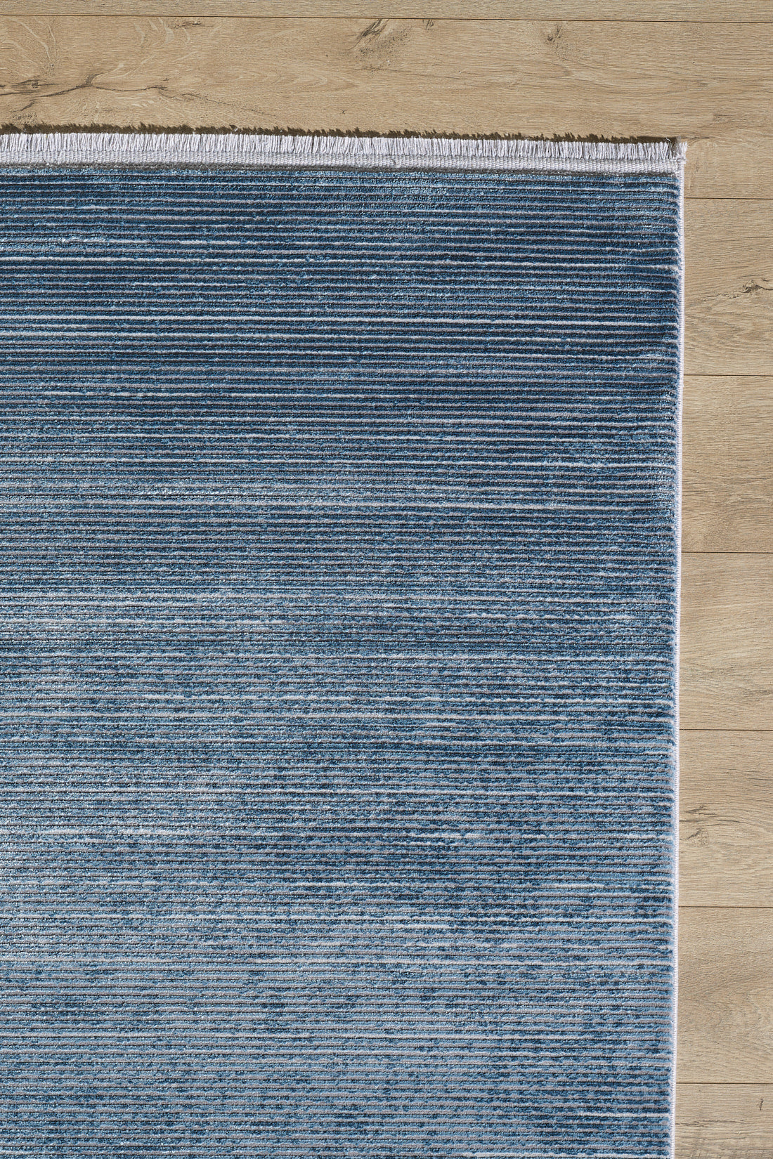 The Slate to Midnight Navy Rug - M497M, a blue rectangular contemporary rug with subtle horizontal stripes and white fringe on one end, is laid on a light wood floor.