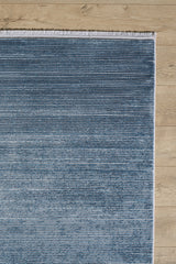 The Slate to Midnight Navy Rug - M497M, a blue rectangular contemporary rug with subtle horizontal stripes and white fringe on one end, is laid on a light wood floor.
