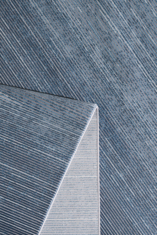 Load image 1 in gallery view. A close-up of the Slate to Midnight Navy Rug - M497M shows blue gradients with diagonal white stripes; one corner is folded to reveal a lighter striped pattern on the underside.