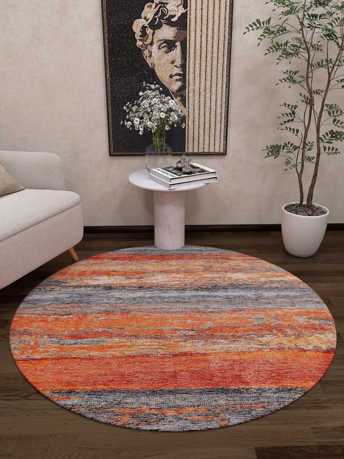 The Sleek Brushed - Washable Rug - JR431, featuring orange with gray and beige stripes, is displayed on a dark wood floor by a white sofa. Ideal for high-traffic areas, it adds cozy style to this modern room with art, books, and plants.