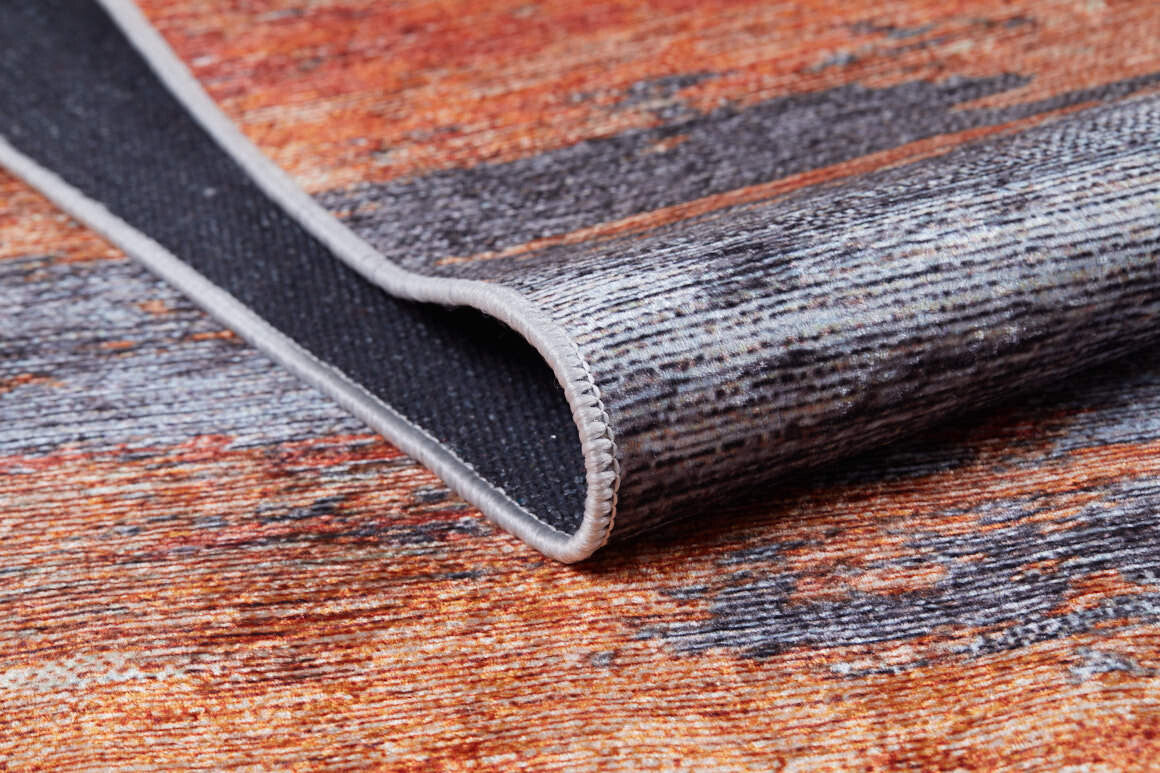 A close-up of the Sleek Brushed - Washable Rug - JR431 (Custom Size) shows its textured surface in orange, brown, and gray with a stitched border, perfect for high-traffic areas. One edge is lifted to display the underside.