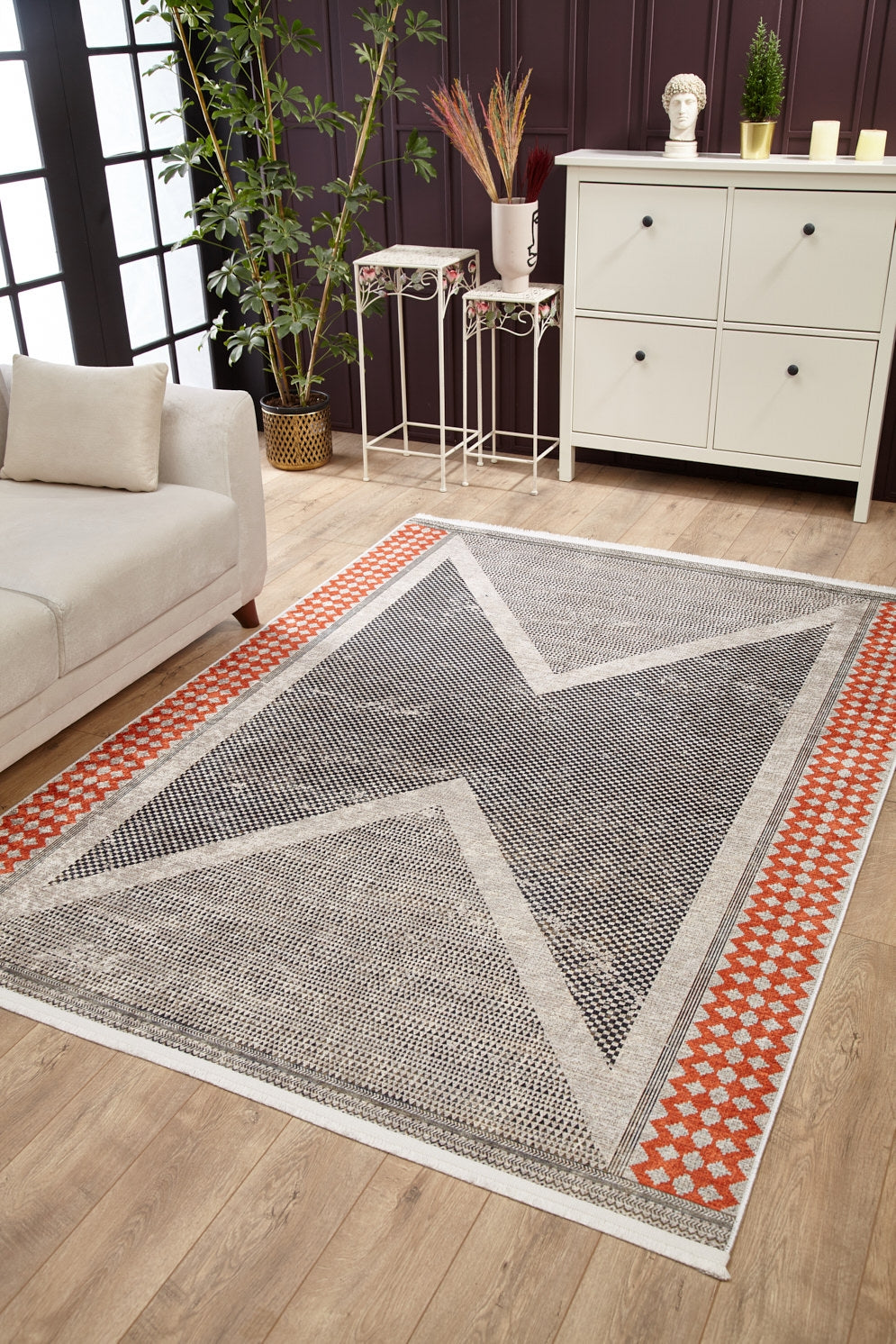 A modern living room with the Sleek Design - Washable Rug - JR1727 (Custom Size), featuring a large gray and black X pattern with a red border—ideal for allergy-sensitive homes. Includes light wood flooring, white storage, sofa, plants, and decor.