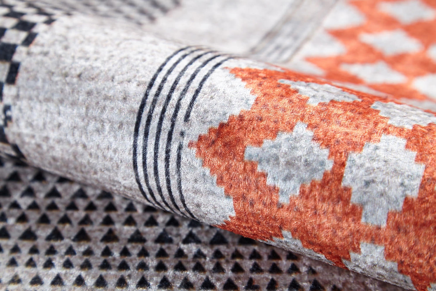 A close-up of the Sleek Design - Washable Rug - JR1727 (Custom Size), showcasing geometric patterns with black and white triangles, orange and gray diamonds, and parallel black lines—perfect for allergy-sensitive homes.