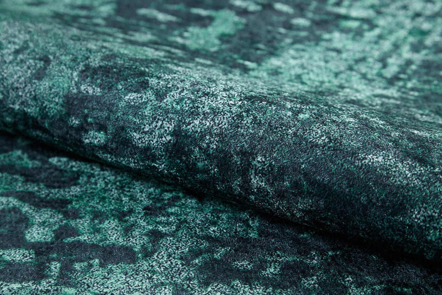 A close-up of the Smokey Mountains - Washable Rug - JR1631 (Custom Size) shows its textured green and black flat weave, featuring a mottled abstract pattern and a slightly raised diagonal fold.