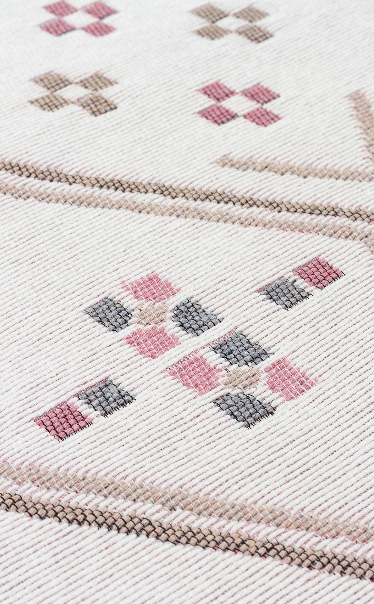 Close-up of the Soft Bloom - Washable Double-Sided Kilims - AR05, a white kilim with pink, brown, and gray geometric X and diamond motifs. Recycled cotton fabric and stitching details are clearly visible. Machine washable for easy care.