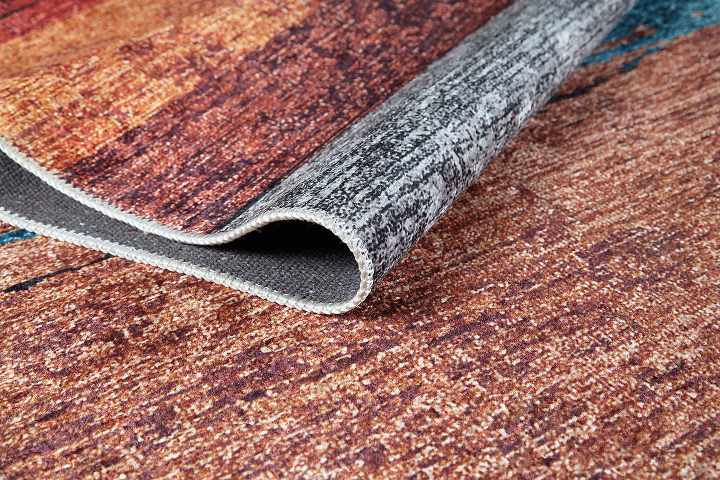A close-up of the Soft Brushed - Washable Rug - JR5056 (Custom Size) in brown, orange, and gray tones, partially lifted to show the underside and detailed weave—ideal for high-traffic spaces.