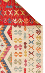 The Soft Mosaic - Kilim - NMD08 is a vibrant multicolour rug with geometric patterns in red, yellow, green, blue, and orange. Its folded corner reveals a red underside featuring X-shaped traditional motifs and striking kilim designs.
