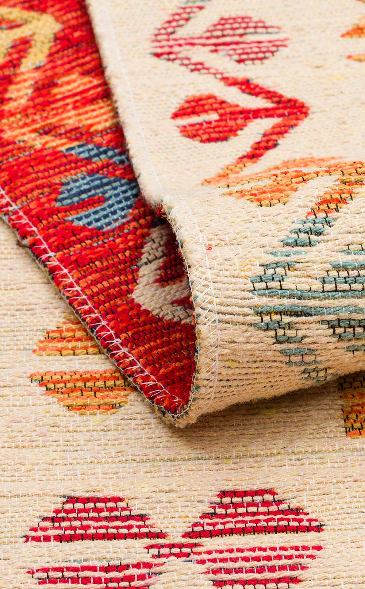A close-up of the Soft Mosaic - Kilim - NMD08 rug showcases its colorful geometric pattern in red, blue, orange, and beige. One edge is folded over, revealing both the front and back textures along with its traditional motifs.