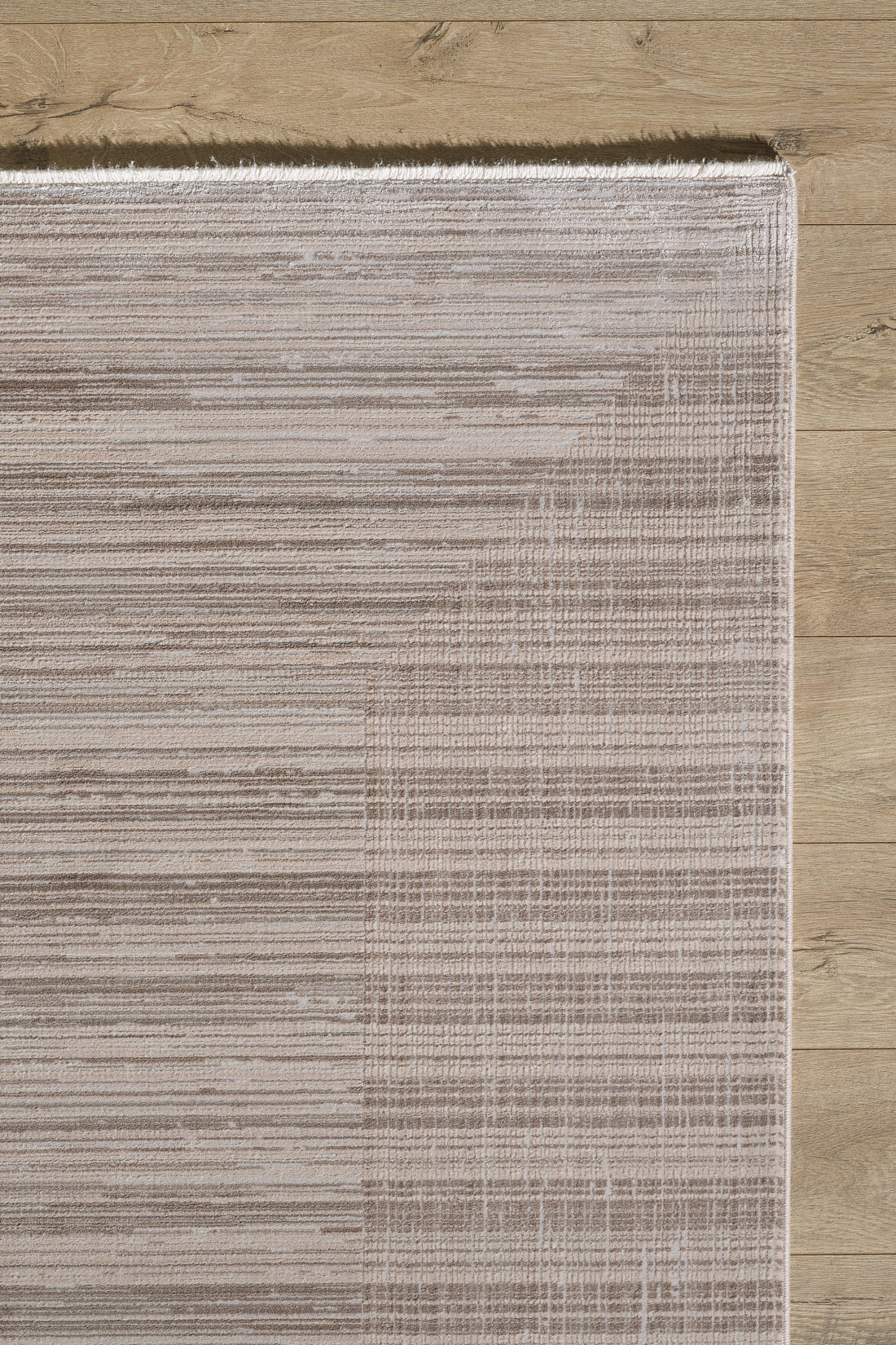 A close-up of the Soft Stripe Serenade Modern Rug - EW2814 in light beige and taupe, featuring a subtle linear pattern and stylish fringed edge, placed on a light wooden floor with its neutral-toned corner visible.