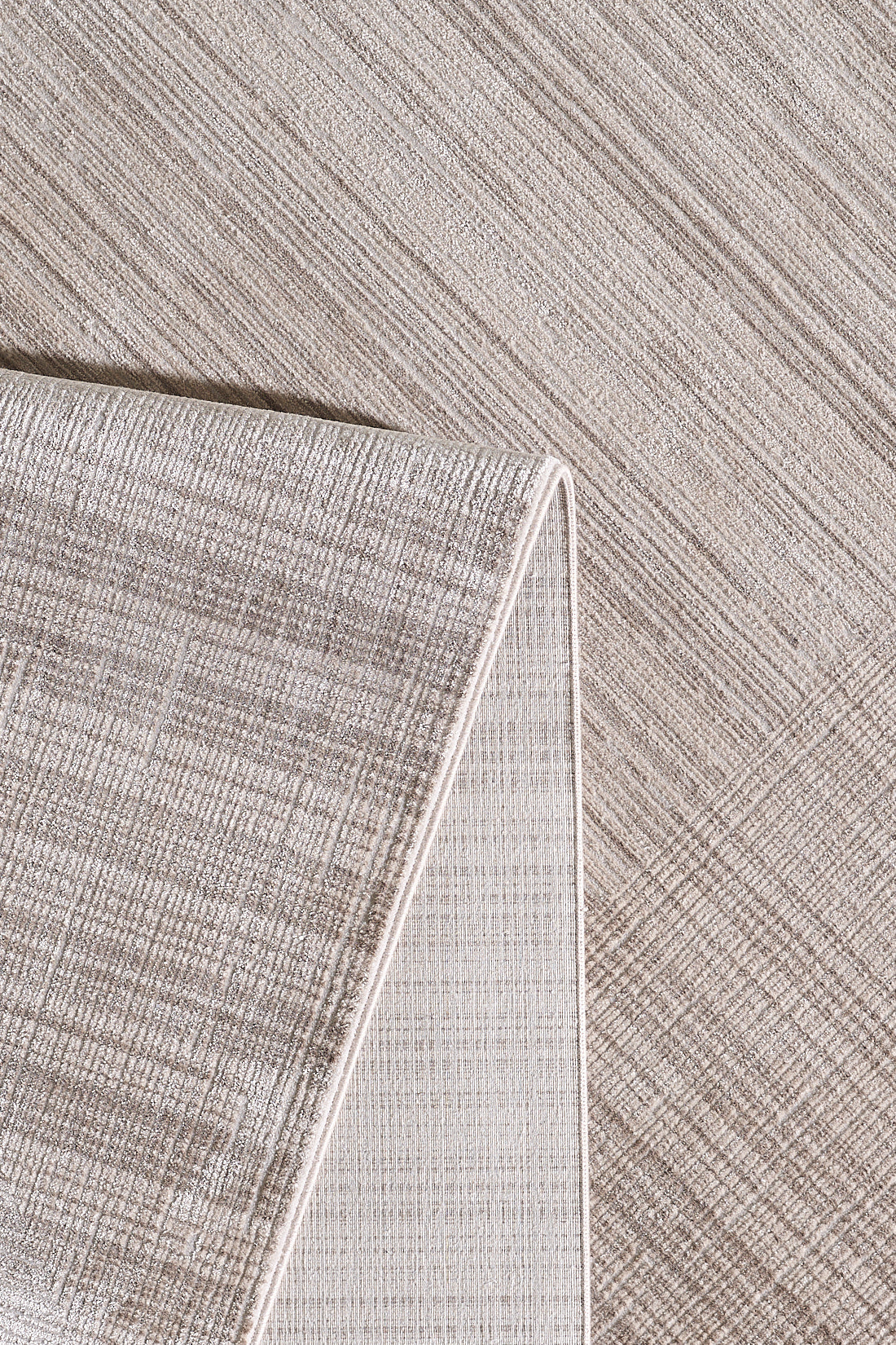 A close-up of the Soft Stripe Serenade Modern Rug - EW2814, featuring neutral tones and a subtle crisscross pattern. Partially folded at the corner, it showcases its textured surface and refined edge detailing for a modern look.