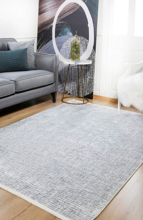 Bild 1 in Galerieansicht laden. A modern living room featuring a gray sofa, the Softly Chic - Washable Rug - JR747 in light gray, a white fur chair, a round side table with a decorative birdcage, and abstract art propped near a bright window.
