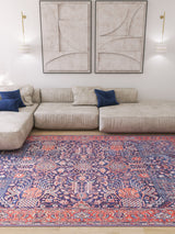 A modern living room with a beige sectional, blue accent pillows, two abstract wall art pieces, wall-mounted lights, and the Solstice Red Navy Washable Rug - LCC3026 with vibrant hues on a wooden floor.