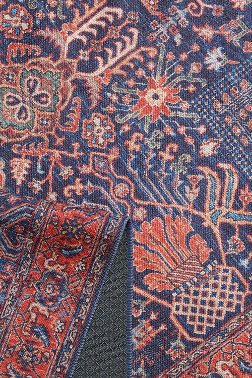 Bild 1 in Galerieansicht laden. A close-up of the Solstice Red Navy Washable Rug - LCC3026 (Custom Size) shows blue with intricate red, orange, and cream floral and geometric designs. The folded corner reveals its textured underside—durable for high-traffic areas and easy to wash.