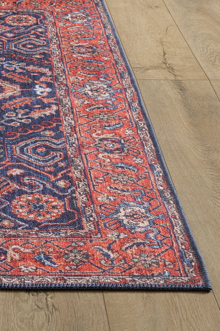 A close-up of the Solstice Red Navy Washable Rug - LCC3026 (Custom Size) with detailed red, blue, and white floral-geometric patterns on a light wood floor—ideal for high-traffic areas. Only part of the rug and floor are shown.
