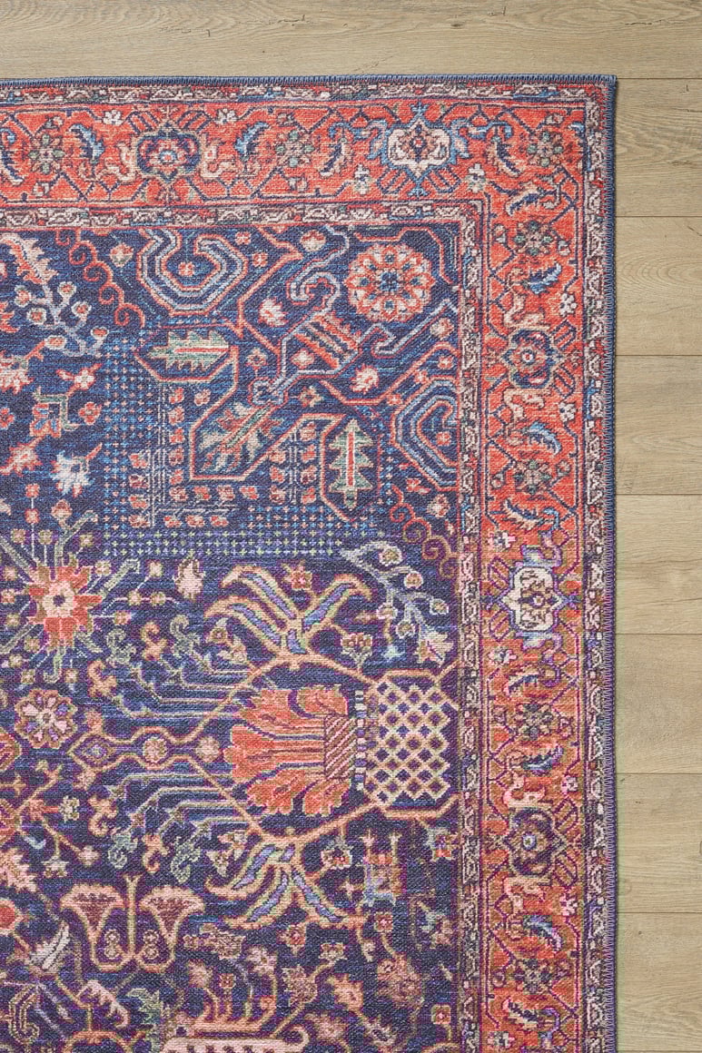 A close-up of the Solstice Red Navy Washable Rug - LCC3026 (Custom Size), featuring ornate floral and geometric patterns in blue, red, and pink on a light wood floor—ideal as a washable rug for high-traffic areas.