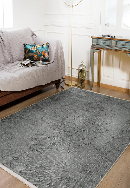 Load image 1 in gallery view. A cozy living room with a brown sofa, a light gray throw, a colorful cushion, the Sophisticated Design - Washable Rug - JR173 (Custom Size) in gray-anthracite for high-traffic areas, a blue vintage console table, floor lamp, white paneled walls, and wooden flooring.