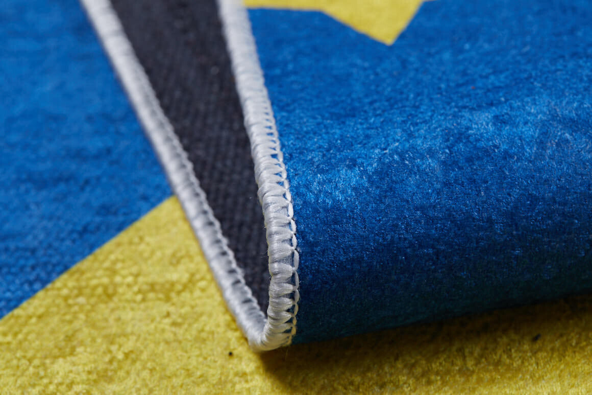 Close-up of the Starry Dreams - Machine-Washable Rug JRC004 (Custom Size), showing its colorful blue, yellow, and black flat weave with white-stitched edges. A lifted corner displays the underside of this washable rug.
