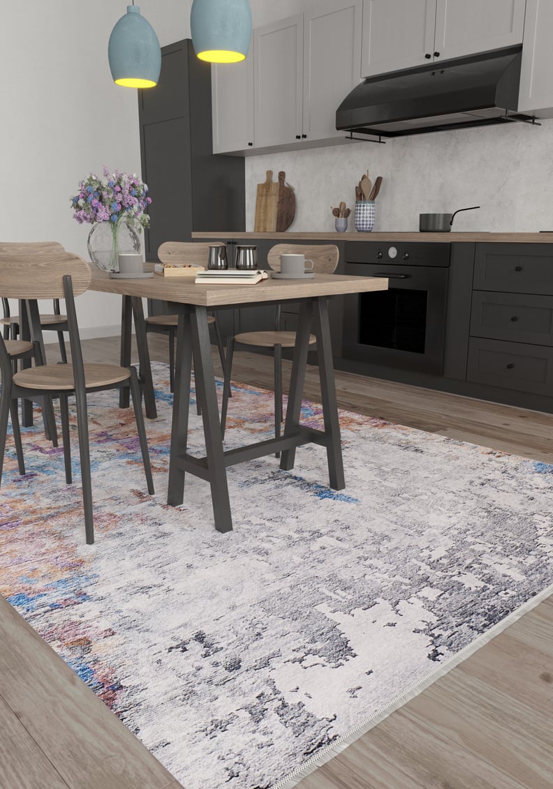 Modern kitchen with light wood dining table and chairs on the Striking Statements - Washable Rug - JR786. Black cabinets, stove, and range hood in the background. Two blue pendant lights hang above a table with a vase of purple flowers.