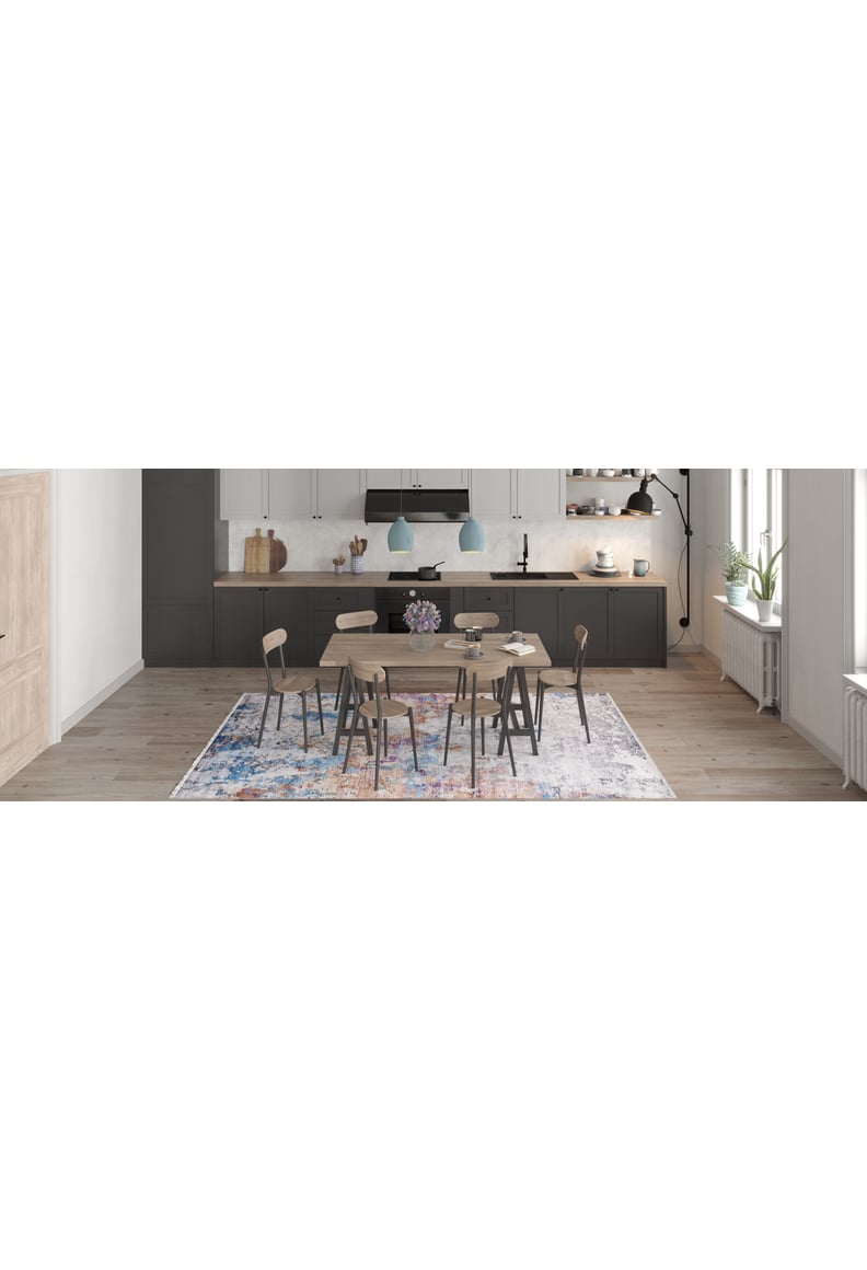 A modern kitchen and dining area with gray cabinets, a wooden table and six chairs, two blue pendant lights, light wood flooring, large windows for natural light, and the Striking Statements - Washable Rug - JR786 (Custom Size) adding color.
