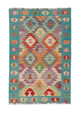 The Striped Elegance - Handwoven Kilim is a rectangular wool rug with colorful geometric patterns in red, orange, purple, blue, green, and cream. It features a teal border with diamond and hexagon shapes and has flatweave construction with fringed edges.