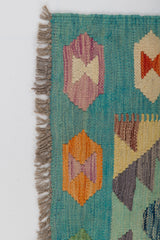 A close-up of the Striped Elegance - Handwoven Kilim, featuring a teal background, orange, purple, and red geometric patterns, and fringed edges on the left side.