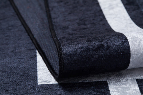 Bild 1 in Galerieansicht laden. Close-up of the Subtle Border - Washable Rug - JR597 (Custom Size) in black with a white geometric pattern; one corner is folded to show its thick, textured build, making it durable and ideal for high-traffic areas.